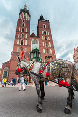 Obraz na płótnie Canvas Church of St. Mary in the main Market Square on the background of dramatic sky and beautiful horse in the foreground. Basilica Mariacka. Krakow. Poland.