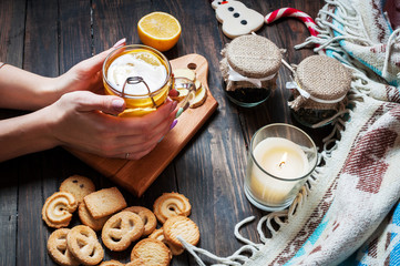 female hands holding cup black tea with lemon, ginger and cookies on dark wood