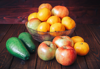 fresh fruit on a table: apples, mandarines and avocado. Dark wood background.