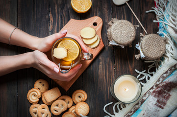 female hands holding cup black tea with lemon, ginger and cookies on dark wood