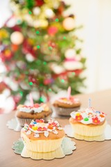 Christmas cup cake on wooden table with decorated Christmas tree