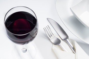 Rotwein im Glas mit Geschirr und Servette auf weißem Tisch
