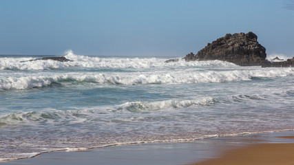 Adraga Beach (Praia da Adraga) in Portugal. Beautiful place, golden sand. Rough sea, rocks, whitewash, blue sky.