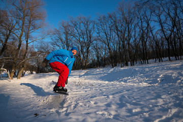 Smiling snowboarder is jumping during riding in the winter fores