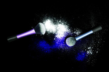 Make-up brushes with colorful powder spilled glitter dust on black background. Makeup brush on new year's Party with bright colors. White and blue powder.