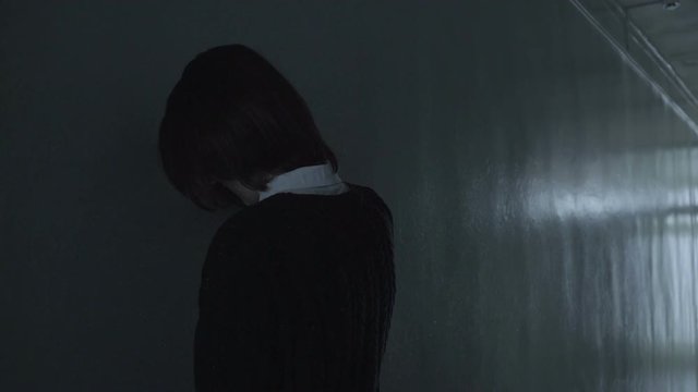 Sad woman facing gray wall in a dull corridor and crying