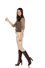 side view of young woman in trousers and high boots posing on white background