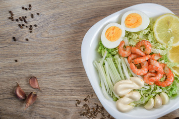 shrimp on a salad with sauce, lemon, egg, garlic cloves in a bowl on a wooden background. Close-up