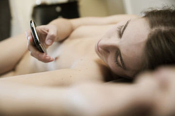 junge Frau liegt nackt auf dem Bett mit einem Smartphone