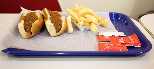 Two simple chili dogs, French fries and condiment packets on a diner tray.