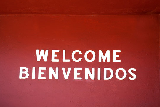 English and Spanish WELCOME BIENVENIDOS sign on red wall. Horizontal.