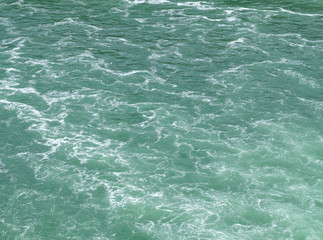 Naturally emerald colored clean and clear water surface with light but very foamy waves flowing down a river after a waterfall. The foam creates a marble looking pattern.