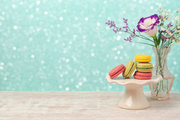 Macarons with flowers on wooden table over bokeh background