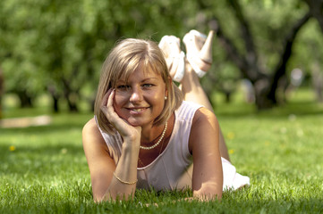 Fototapeta premium Young blond woman in white dress lying on the grass 