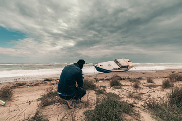 Uomo fotografo di fronte a una barca di immigrati clandestini arenata sulla spiaggia. Fotografie...