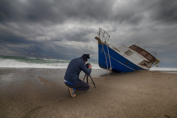 Uomo fotografo di fronte a una barca di immigrati clandestini arenata sulla spiaggia. Fotografie...