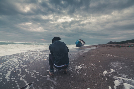 Uomo fotografo di fronte a una barca di immigrati clandestini arenata sulla spiaggia. Fotografie estreme concetto.