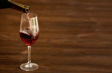 Red wine pouring into a glass on wooden background