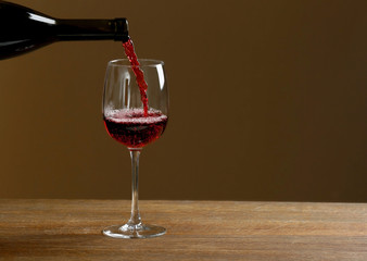 Red wine pouring into a glass on wooden table