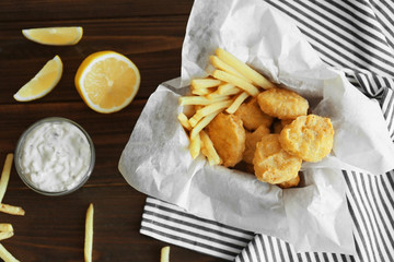 Tasty chicken nuggets with fries, sauce and lemon on table
