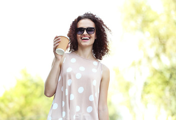 Young cheerful woman with cup of coffee walking in the park