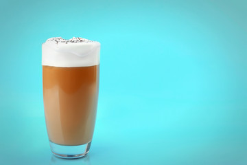 Glass of coffee with cream foam and cocoa powder on blue background