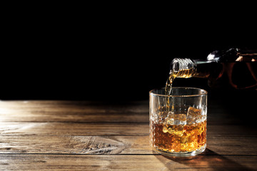 Verser le whisky dans le verre sur le plan rapproché de table en bois