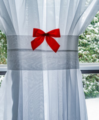 Red Chrismas Bow on White Curtain with window pane and snowy tre