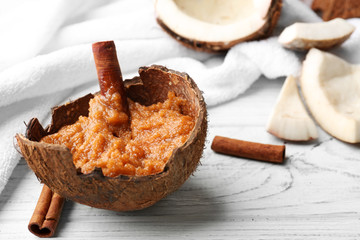 Body scrub with cinnamon stick in coconut shell on wooden background