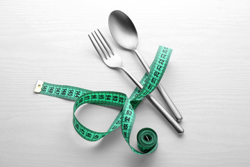 Fork and spoon with measuring tape on white wooden background