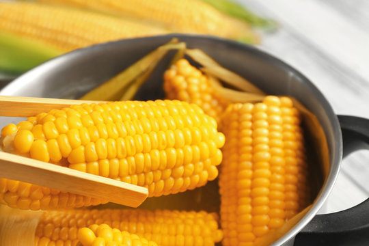 Wooden tongs taking tasty boiled corncob from saucepan, close up