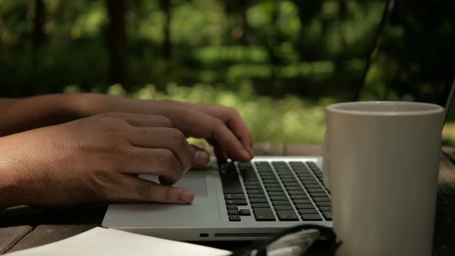 Freelancer man working on computer laptop in the park green nature background.