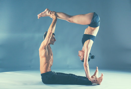 Young couple practicing acro yoga on mat in studio together