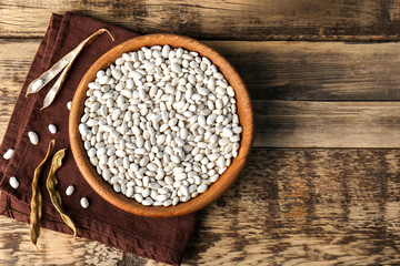 Bowl with white haricot beans and napkin on wooden table