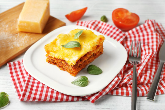 Plate with delicious lasagna and napkin on table