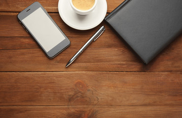 Phone, notepad and cup of coffee on wooden background