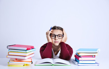 Teenage girl with pile of books sitting at table on white background