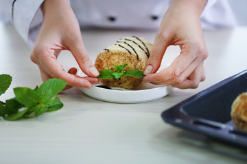 Female hands decorating delicious dessert with mint on kitchen table