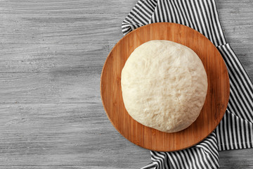 Wooden board with raw dough on kitchen table