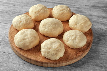 Wooden board with balls of raw dough on kitchen table