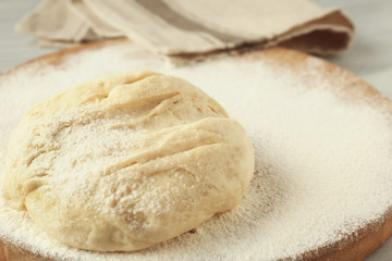 Wooden board with raw dough and flour on kitchen table