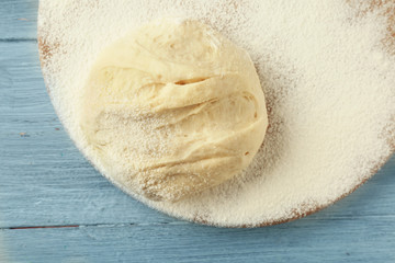 Wooden board with raw dough and flour on kitchen table