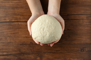 Female hands holding raw dough on wooden background