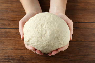 Female hands holding raw dough on wooden background, close up