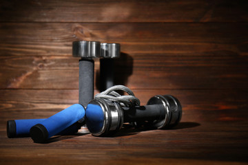 Dumbbells and skipping rope on wooden background