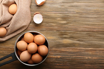 Raw eggs in saucepan on wooden table