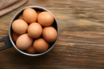 Raw eggs in saucepan on wooden table