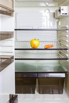 A yellow apple and a carrot on a shelf in a refrigerator