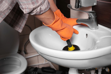 Plumber repairing sink with hand plunger, closeup