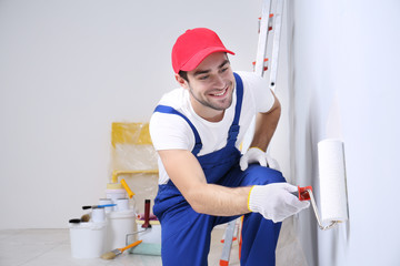 Young worker painting wall in room